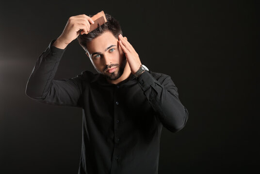 Handsome man combing hair on dark background