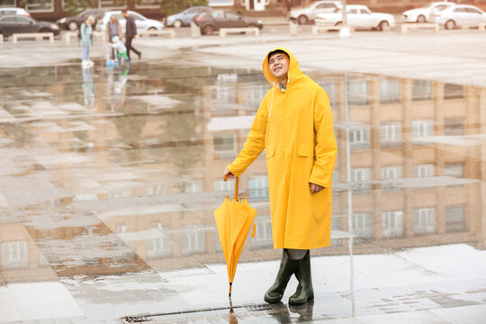 Young Asian Man In Raincoat And With Umbrella On City Street