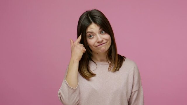 Insane idea! Displeased brunette young woman showing stupid gesture, looking disappointed with senseless dumb suggestion, accusing bad mind, crazy plan. indoor studio shot isolated on pink background