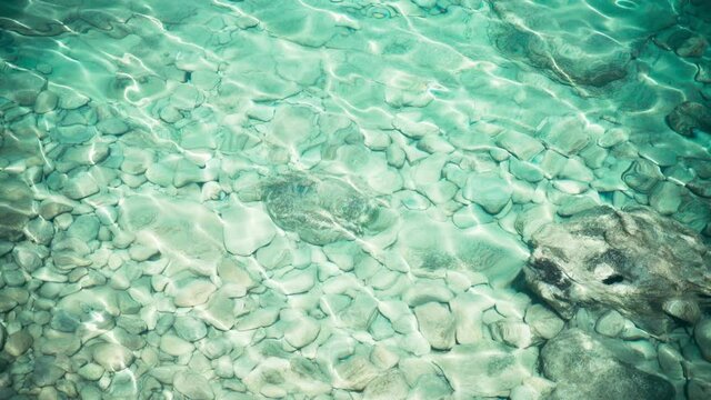 Transparent turquoise blue sea water, top view. Sun glare on the surface and stones at the bottom. High quality 4k footage