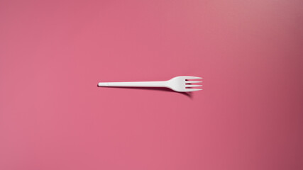 Single plastic fork on a pink background. Top view