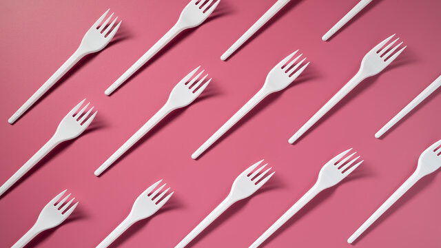 DIAGONALLY: Many plastic forks on a pink background. Top view