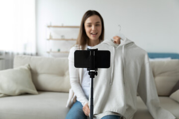 Smartphone on tripod view, woman record video advertisement. Young female designer represent new collection showing to camera white hoodie during online live stream, sell clothes via internet concept