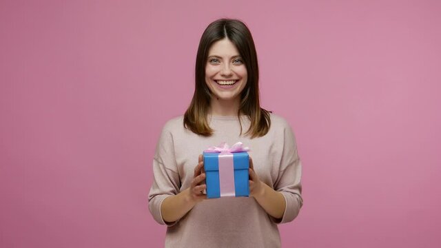 Charming woman catching wrapped present and giving box to camera, sharing christmas gift smiling friendly, celebrating holidays, congratulations on birthday. studio shot isolated on pink background