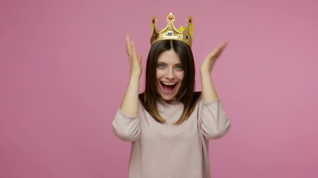 I'm the best! Selfish brunette woman wearing golden crown, feeling confident arrogant, proud of her beauty and success, self-loving egoism concept. indoor studio shot isolated on pink background
