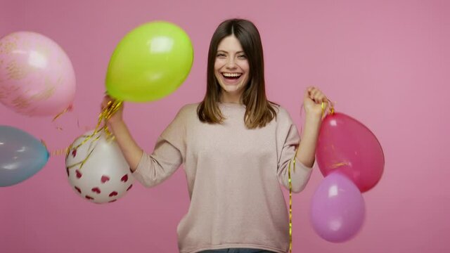 Cheerful happy energetic brunette woman laughing and dancing with colorful air balloons, enjoying birthday party, celebrating holiday, festive mood. indoor studio shot isolated on pink background