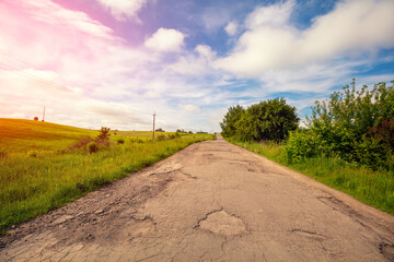 Old country road in potholes and holes. Rural landscape on a sunny day.