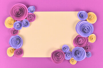 Romantic flower flat lay with blank beige paper surrounded by pink, violet and yellow romantic paper craft roses on pink background