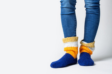 Women's legs in jeans and warm multi-colored socks on a light background