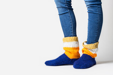 Women's legs in jeans and warm multi-colored socks on a light background