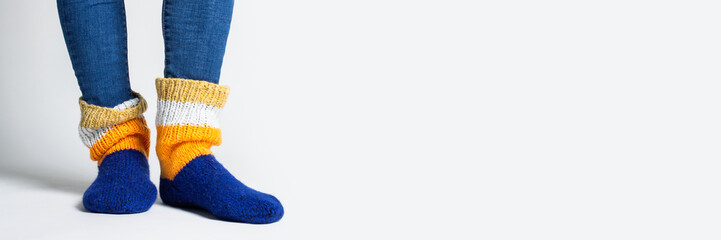 Women's legs in jeans and warm multi-colored socks on a light background