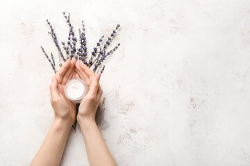 Hands of young woman with cream and lavender on light background