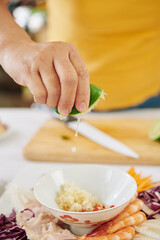 Close-up image of woman squeezing half of fresh lime into bowl with diced garlic and paprika