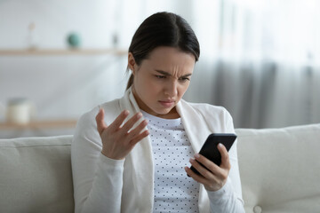 Irritated woman sit on couch holding smart phone feels annoyed network wi-fi connection lost, slow...