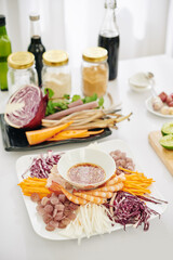 Big plate with boiled shrimps and cut vegetables around bowl with dipping sauce