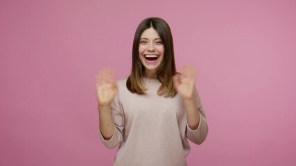 Lovely amiable brunette young woman waving hand to camera, greeting with hello gesture and smiling, welcoming saying hi with friendly expression. indoor studio shot isolated on pink background