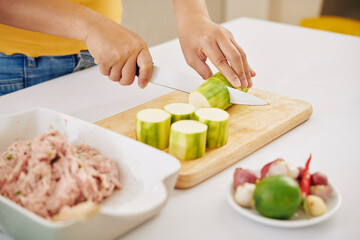 Hands of woman cutting zuccini with sharp knife on wooden board