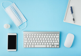Bright blue modern desk with medicine mask and sanitizer. Top view. Social distance in office.