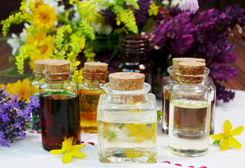 Selection of  glass aromatherapy essential oil bottles, with herbs and flowers in the background