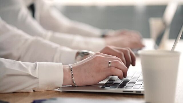 close up of two businesspeople typing on laptop computers in row. professional men worker in white shirt. concept coffee cup, computing, device. modern employees