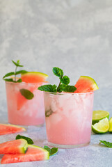 Two pink summer drinks with watermelon and lime. With crushed ice, and garnished with a mint twig.