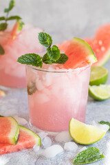 A pink summer drink with watermelon and lime. With crushed ice, and garnished with a mint twig.