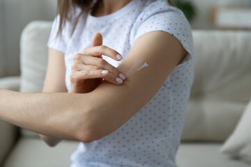 Close up view woman sitting on couch applying cream on arm caring about skin prevent dryness using...