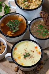 hot soups in mugs on wooden tray, vertical top view