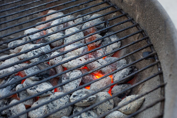 A view looking into a kettle barbecue. Glowing embers and gray charcoal provide heat for food.