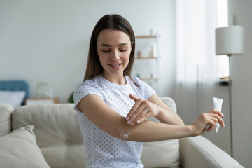 Woman sit on sofa in living room holding small tube with serum caring about skin beauty health care...