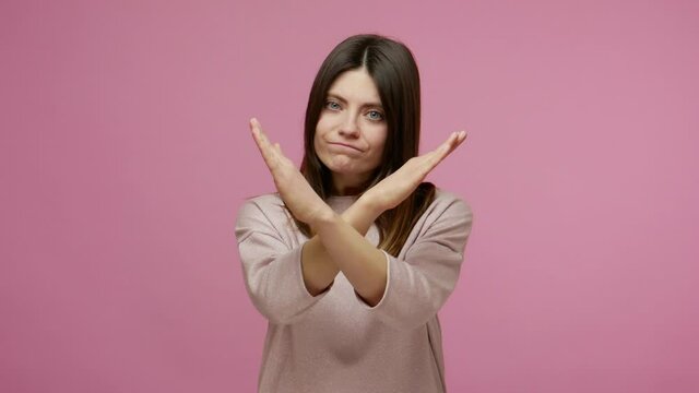 No way, this is finish! Brunette woman crossing hands in stop gesture, definitely rejecting suggestion, warning of trouble, declining with negative expression. studio shot isolated on pink background