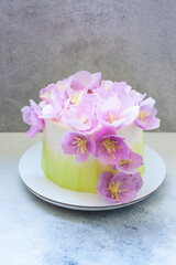 Fototapeta na wymiar Tender green birthday cake with purple and pink paper flowers on grey background.