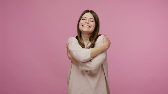 Amazing very beautiful girl with kind smile embracing herself with pleasure expression, proud of own gains, demonstrating self-love, positive self-esteem. studio shot isolated on pink background