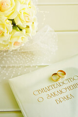 Golden wedding rings,marriage certificate and bride bouquet on a table of light wood. 1.