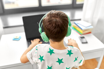technology, gaming and people concept - boy in headphones with laptop computer at home