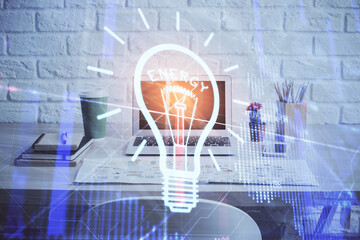 Computer on desktop in office with bulb icon hologram. Double exposure. Concept of idea.