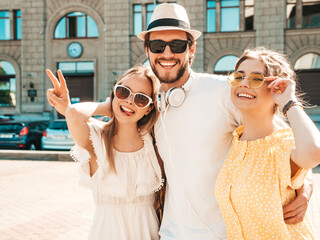 Group of young three stylish friends posing in the street. Fashion man and two cute girls dressed in casual summer clothes. Smiling models having fun in sunglasses.Cheerful women and guy going crazy