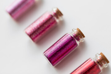 party, decoration and holidays concept - close up of glitters of different red and pink shades in small glass bottles with cork stoppers over white background