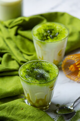 Hot green tea in a glass with cream topped with green tea, decorated with green tea powder.