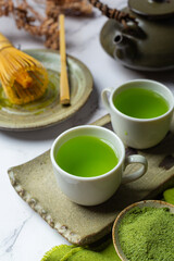 Hot green tea in a glass with cream topped with green tea, decorated with green tea powder.