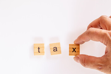 Businessman hand creates the word "tax" of the wooden letter blocks on white background.