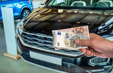 hand holding euro banknotes, car on background