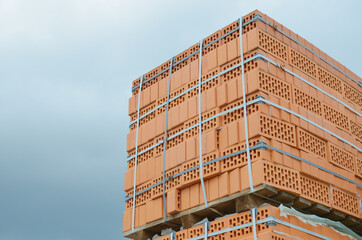 A tied bundle of lightweight red bricks against a blue cloudy sky closeup outdoors, on a wooden pallet.