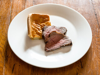 home-made sliced Roast Beef and piece of Yorkshire pudding on white plate on old wooden table at home kitchen
