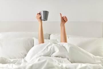 morning, comfort and people concept - young woman with cup of coffee lying in bed and showing...