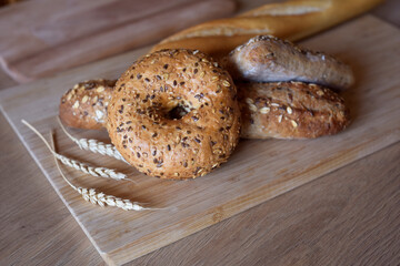 Different types of bread, fresh pastries in the bakery. Bread with sesame seeds, cereals, seeds. Different forms and types of rolls. Wheat ears on a wooden board