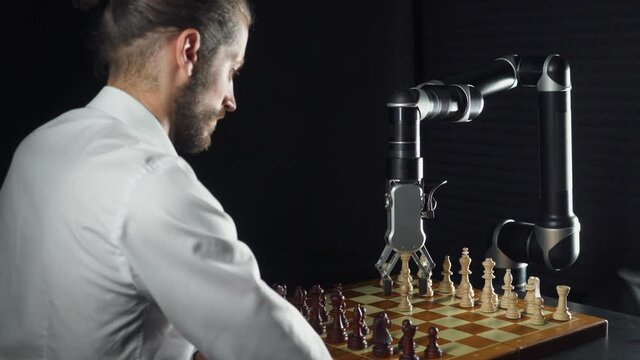 Competition, man playing chess with a robot, the confrontation between man and artificial intelligence, futuristic robotic arm participates in the game, black background.