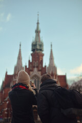 Fototapeta na wymiar A couple traveling to Krakow takes a photo on the phone. The cold season. Couple makes photo of church in historical city