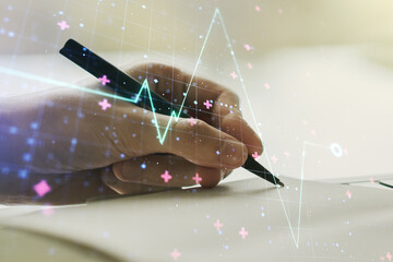 Creative abstract heart pulse hologram and man hand writing in diary on background, online medical...