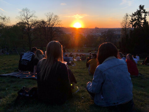 A young crowd watching the sun set over the castle from Riegrovy Sady Park